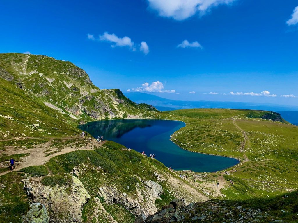 green and gray mountain beside blue lake under blue sky during daytime